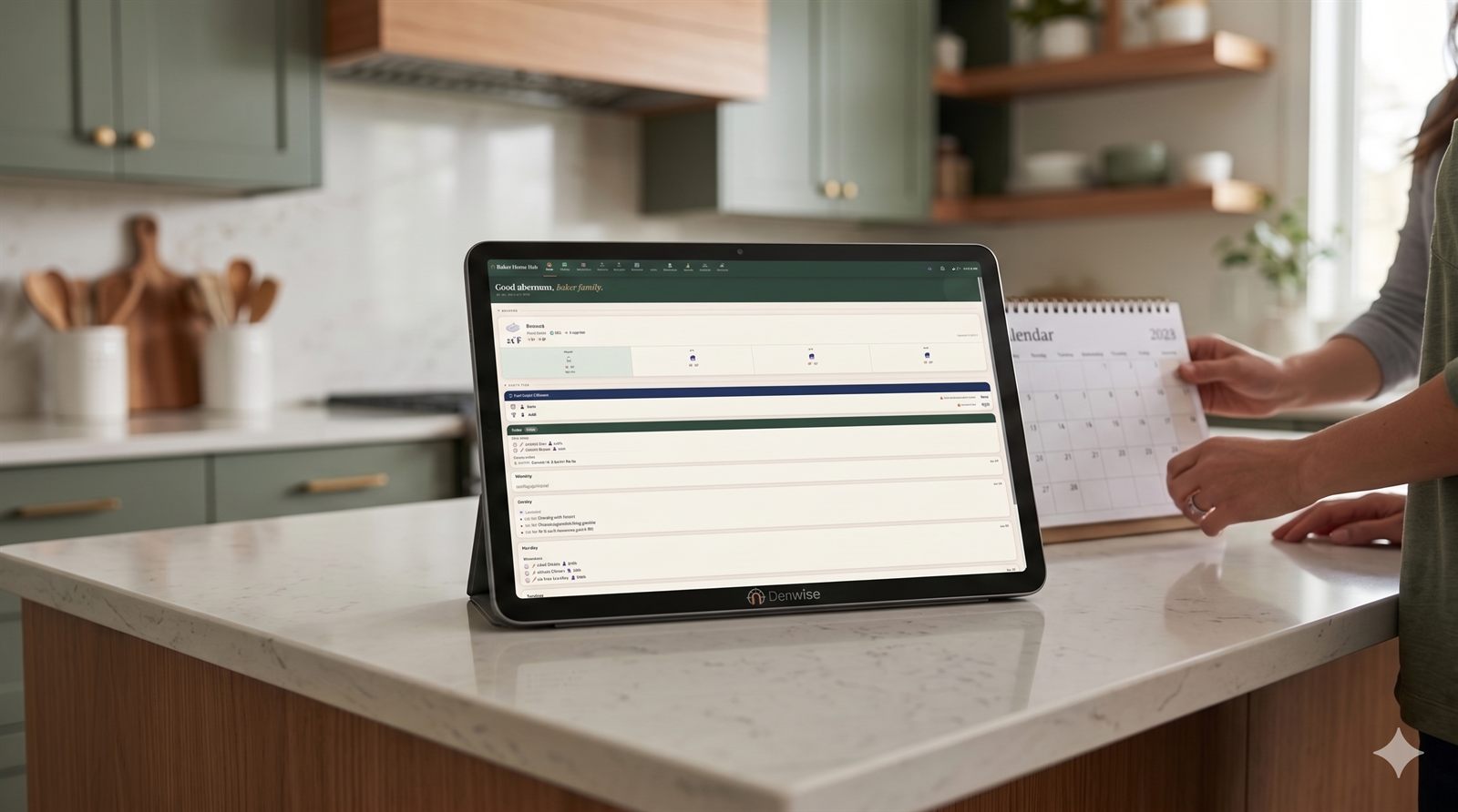 The Denwise dashboard on a tablet in a modern family kitchen, beside a wall calendar